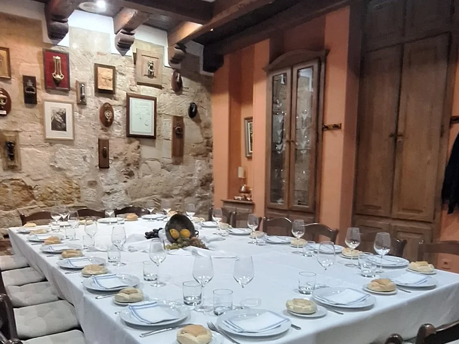 El comedor de La Aldaba con una mesa larga puesta, la pared de piedra llena de aldabas y vigas de madera