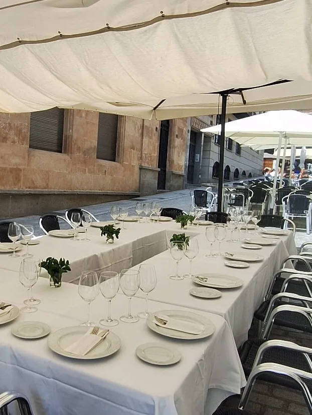 Terraza de La Aldaba bajo los toldos, con mesas largas puestas con mantel blanco, en la calle Felipe Espino